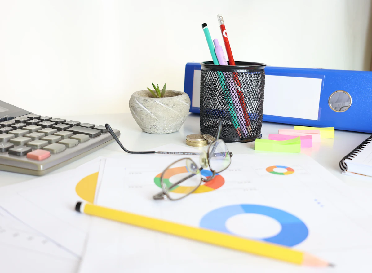 Schreibtisch mit Taschenrechner, Brille, Ordner und Diagrammen